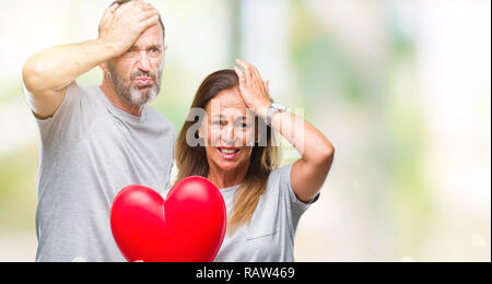 Medioevo ispanico casual giovane in amore azienda cuore rosso su sfondo isolato ha sottolineato con la mano sulla testa, sconvolto con vergogna e la sorpresa di fronte, Foto Stock