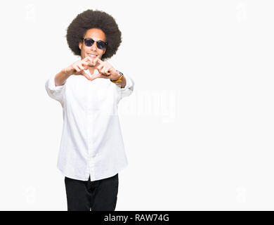 Giovane americano africano uomo con capelli Afro indossa occhiali da sole sorridente in amore che mostra il simbolo del cuore e la forma con le mani. Concetto romantico. Foto Stock