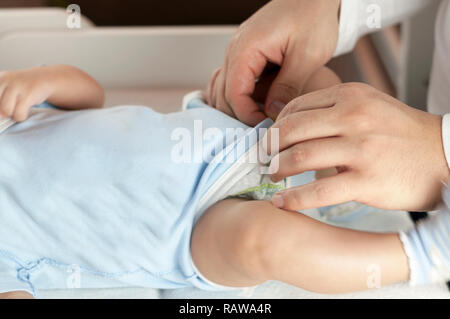 Giovani papà cambia il pannolino e vestiti per il suo neonato bambino piccolo. Messa a fuoco selettiva Foto Stock