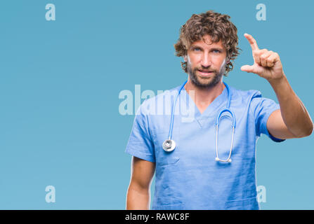 Bello ispanica medico chirurgo uomo sullo sfondo isolato sorridente e fiducioso gesticolando con la mano facendo segno di dimensione con le dita mentre cercano e Foto Stock