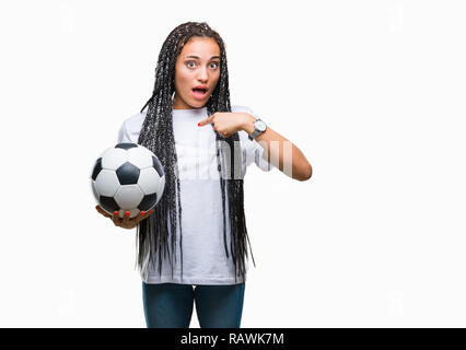 Giovani capelli intrecciati African American Girl tenendo palla calcio su sfondo isolato con sorpresa faccia puntare il dito a se stesso Foto Stock