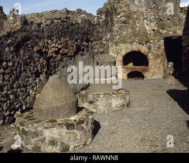 L'Italia. Pompei. Panetteria (Pistrium). Vista la costituzione. Macine in basalto lavico, pilotato da asino per macinare il grano, il forno per il pane e il camino del forno. Campania. Foto Stock