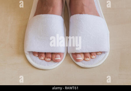 Primo piano vista superiore della coppia di nuovo bianco pantofole in camera dell'hotel. Donna con bella french bianco e rosa pedicure fresco. Colore orizzontale fotografi Foto Stock