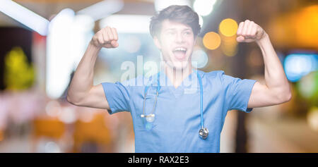 Giovane medico medico che indossano uniformi su sfondo isolato che mostra i muscoli di armi sorridente fieri. Concetto di fitness. Foto Stock