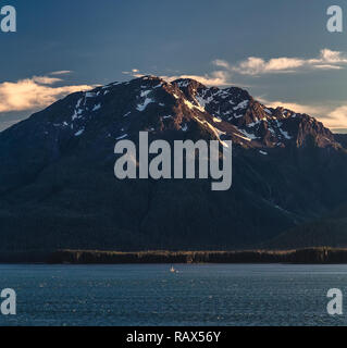 Imponente montagna al tramonto con una piccola barca a vela in Alaska Foto Stock