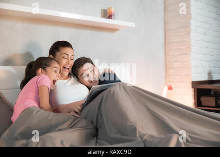 Una madre caucasica e i suoi figli guardare un film divertente su un tablet mentre nel letto. Figlia della madre e figlio del tempo di qualità. Tempo per la famiglia. Il tempo del filmato. 4k UHD Foto Stock