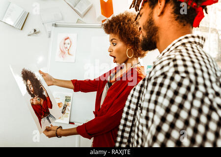 Attraente sentimento donna molto sorpreso vedendo il suo straordinario ritratto Foto Stock