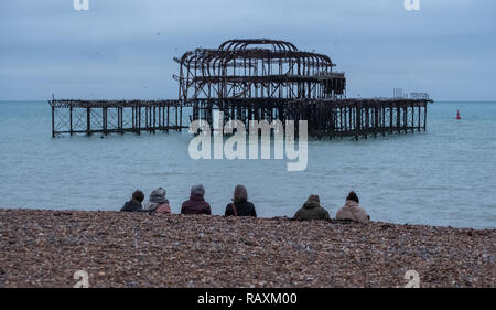 Fila di donne seduto sulla spiaggia ghiaiosa di Brighton Regno Unito, su un inverno di pomeriggio a dicembre, davanti alle rovine del Molo Ovest. Foto Stock