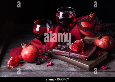 Fresco di succo di melograno in bicchieri di vino nei pressi di frutti, libri e donna nera sulla maschera in legno rustico sfondo con spazio per il testo Foto Stock