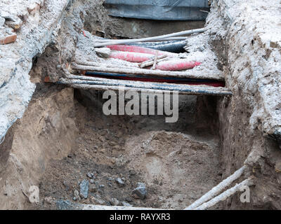 Tubi di acqua e fili elettrici nel suolo fossa fossa di trincea durante il plumbing in costruzione riparazione. L'immagine orizzontale Foto Stock