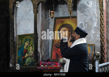 Ortodossa Etiope di Monaco in preghiera dentro la Chiesa Copta Cappella di San Michele Arcangelo nella sezione inferiore di Deir El-Sultan monastero etiope che si trova sul tetto della chiesa del Santo Sepolcro nella città vecchia di Gerusalemme Est Israele Foto Stock