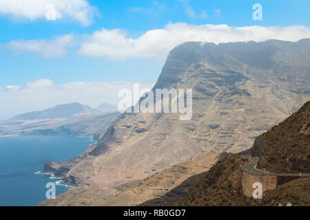 Road Trip opinioni su una strada costiera con enormi catene montuose sullo sfondo a destra vicino al mare / Oceano atlantico (Gran Canaria, Spagna, Europa) Foto Stock