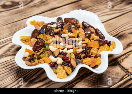 Piatto di frutta secca sulla tavola di legno, Mix di frutta e bacche: anacardi, nocciole, mandorle, giallo, marrone e blu di uvetta uvetta, mirtilli rossi secchi Foto Stock