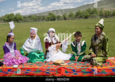 Famiglia kazako in abiti tradizionali con una donna cantare e suonare strumento locale di dombra, Kazakistan. Foto Stock