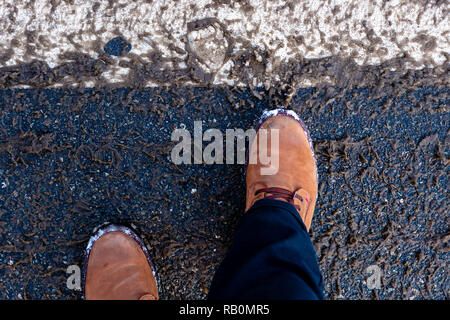 Mans piedi in scarpe invernali sulla neve sporca per le strade. Foto Stock