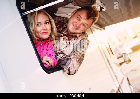 Sposati di mezza età giovane famiglia moglie e marito uscendo dalla roulotte veicolo ricreativo motor home finestra rimorchio guardando la fotocamera Foto Stock
