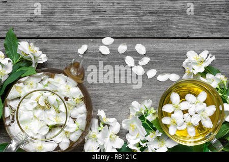 Tazza di tè con fiori di gelsomino e teiera su un sfondo di legno. vista superiore Foto Stock