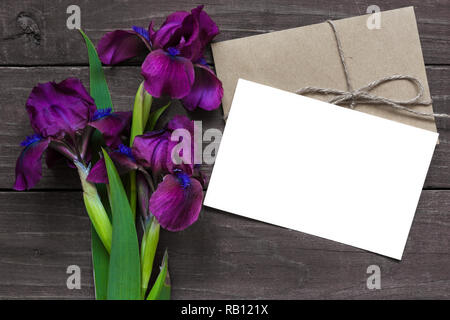 Vuoto bianco della scheda Messaggi di saluto e la busta con il viola iride fiori mockup in scuro legno rustico sfondo per il lavoro creativo design. vista superiore. laici piatta Foto Stock