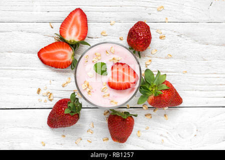 Yogurt alla fragola in un vetro con frutti di bosco freschi, avena e menta bianca su sfondo di legno. Colazione sana. vista superiore Foto Stock