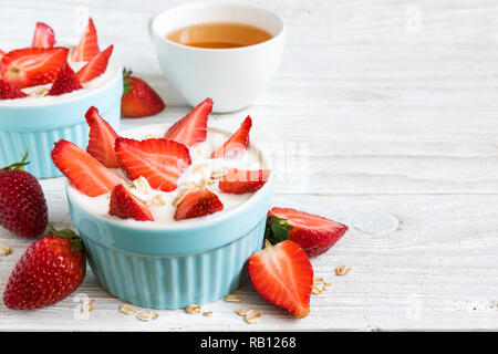 Un sano di yogurt alla fragola con frutti di bosco freschi e avena su bianco tavolo in legno è servito per una sana prima colazione. close up con spazio di copia Foto Stock