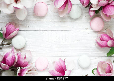 Cornice fatta di rosa fiori di magnolia con macarons su bianco tavolo in legno. mock up. flat laici. vista dall'alto. il matrimonio o la festa della mamma sfondo Foto Stock