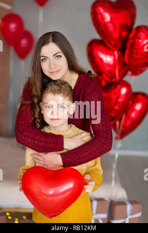 Bella carino bruna giovane madre mom con il suo ragazzo bello ragazzo azienda ogni altro e felici insieme.donna in penne di colore giallo e rosso dolce Foto Stock