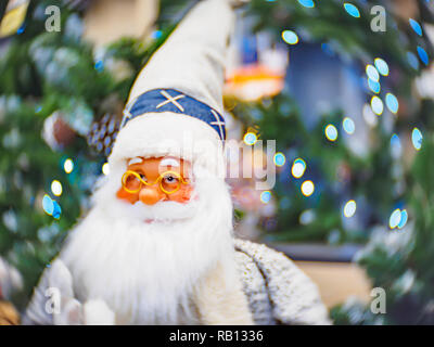 Toy Santa Claus in piedi contro un festoso illuminato soft focalizzato sullo sfondo bokeh di fondo. Natale e Anno Nuovo concetto. Foto Stock