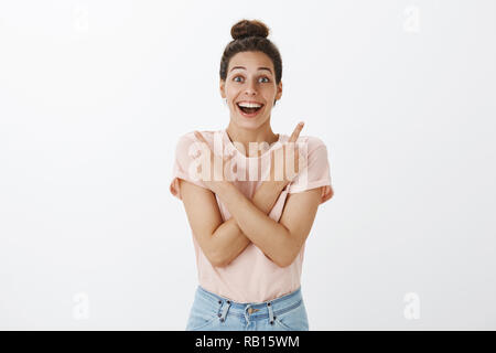 Ritratto di felice e impressionato bella sorpresa donna rivolto lateralmente come bracci di incrocio sul petto, mostrando di destra e di sinistra e facendo reagire divertito su grandi prodotti in vendita, sorridente Foto Stock