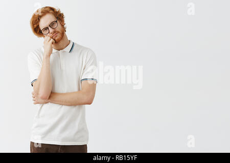 In attesa di bella redhead fidanzato con barba faccia pendente sul pugno e testa tiltante guardando con calma e espressione indifferente al sentimento della fotocamera annoiato o stanco su sfondo grigio Foto Stock