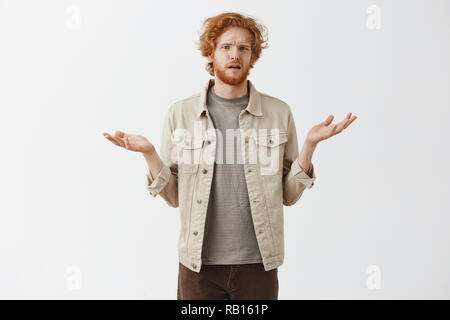 Confuso confuso e disordinato funny redhead giovane maschio in camicia al di sopra striped t-shirt scrollare con diffusione palme e clueless espressione avente la più pallida idea di dove si è svegliato dopo aver bevuto tutta la notte Foto Stock