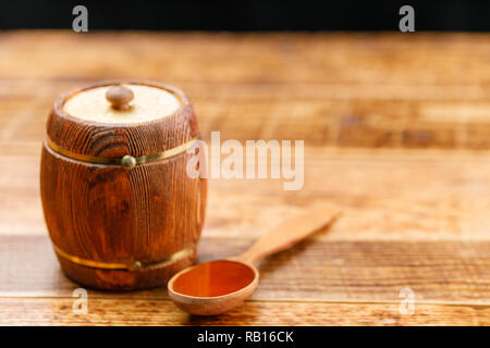 Chiuso il barile con il miele e il cucchiaio di legno su una tavola di legno. Canna. Close-up. Foto Stock