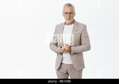 Ritratto di smart e bello senior intelligente professore maschio in abito elegante e occhiali tenendo le mani insieme contro il petto e guardando con auto-assicurato espressione saggio in telecamera dare la parola Foto Stock