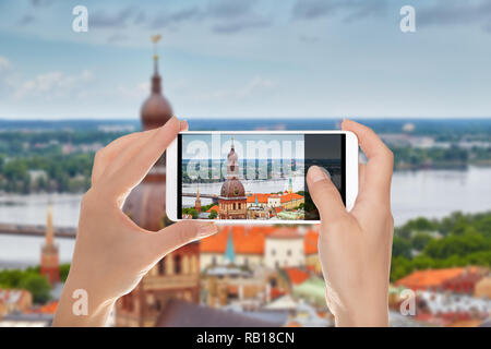 Un uomo è fare una foto della vista della città di Riga da sopra, inclusi la Torre della cattedrale del Duomo su un telefono cellulare Foto Stock