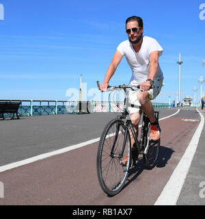 Uomo in 20s o 30s in bicicletta lungo una pista ciclabile sul lungomare di Brighton, East Sussex, Inghilterra, Regno Unito. Foto Stock