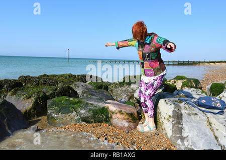 Trendy ben vestito giovane cerca donna senior di camminare su una spiaggia di ciottoli sulla ghiaia e rocce nel Regno Unito. Foto Stock