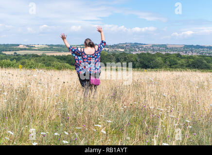 Giovane donna salti di gioia in un prato nella campagna britannica, UK. Correre e saltare. Felice concetto. Braccia in alto. Il salto di un campo. Foto Stock