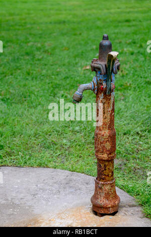 Un ritratto di una verticale e in vecchio stile rustico fontana di acqua realizzato in ferro, con molti punti di ruggine Foto Stock