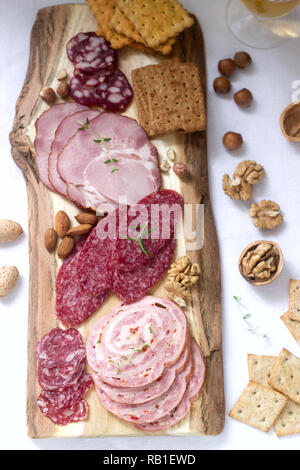 Antipasto di vari tipi di salumi, carni, formaggi e crackers su una tavola di legno, servita al vino. Foto Stock