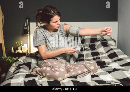 L'argomento di alta pressione sanguigna di ipertensione malattia. 22 anno di età giovane donna caucasica utilizza il tonometro automatico. Lei mette il bracciale sul braccio controllare pressur Foto Stock