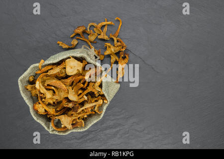 Vista superiore della composizione secca di funghi finferli collocato in borsa di tela sulla pietra nera superficie di sfondo con spazio di copia Foto Stock