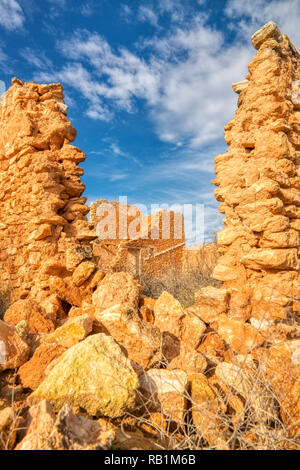 Una foto verticale delle rovine di una vecchia casa di pietra guardando attraverso la rottura di una parte della parete in corrispondenza di un'altra parte della casa con un cielo blu e nuvole Foto Stock