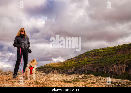 Una donna bionda e la sua bionda Border Collie cane godendo la vivace aria di montagna in autunno a Cuenca in Spagna con moody nuvole a distanza Foto Stock