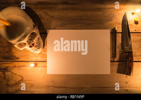 Cranio umano con la luce di una candela e libro bianco con la matita e il coltello sul tavolo in legno e decorate per tema Halloween con copia spazio. Foto Stock