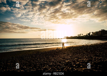Matura in amore bacio con sorprendente colorato tramonto d'oro in background. La spiaggia e l'oceano onda luogo scenico in Tenerife. romantico e tenerezza conce Foto Stock