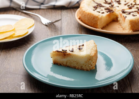 In casa la cheesecake cosparso con scaglie di cioccolato su una piastra di blu. Sfondo di legno, vista laterale Foto Stock