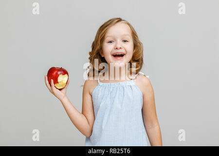 Ritratto di un sorridenti piccola bionda bambino ragazza con un morso apple rosso su sfondo grigio Foto Stock