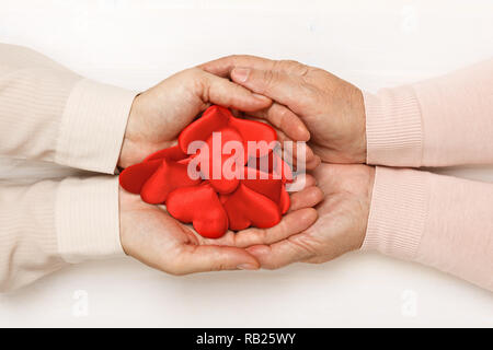 Close-up della mano di un adulto figlia e una vecchia madre, tenendo insieme molti cuori nel loro palmi. Vista dall'alto. La famiglia e il concetto di cura Foto Stock