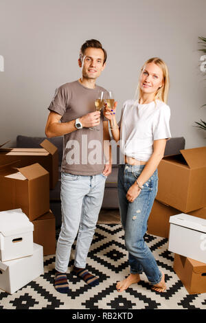 Foto della giovane coppia con bicchieri di vino in piedi tra le scatole di cartone Foto Stock