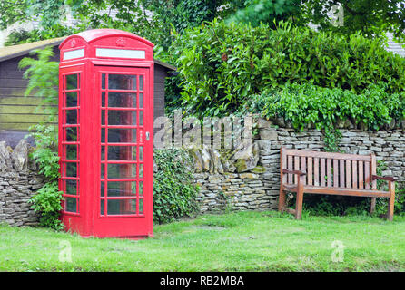 Red classic box telefonico da una panca in legno in un villaggio comune, inglese paesaggio rurale . Foto Stock