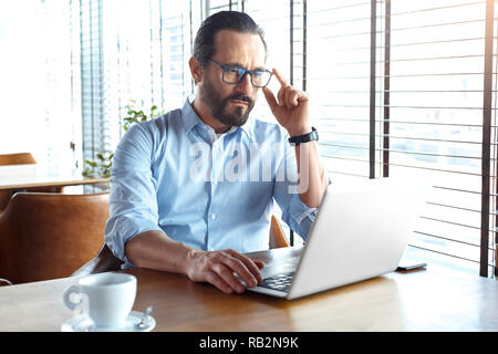 Business Lifestyle. Commerciante in bicchieri seduto al caffè con caffè di lettura dei grafici di trading su laptop gravi Foto Stock